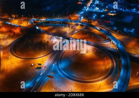 Städtisches Verkehrskonzept. Straßenautobahnen und Kreuzungen bei Nacht mit Auto- und LKW-Verkehr, Luftaufnahme von Drohne. Stockfoto