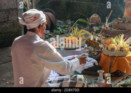 Rückansicht des hinduistischen Priesters, der während einer Hochzeitszeremonie betet. Pedanda sitzt auf dem Boden vor den Opfergaben und führt Hochzeitszeremonien durch Stockfoto