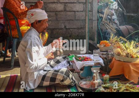 Rückansicht des hinduistischen Priesters, der während einer Hochzeitszeremonie betet. Pedanda sitzt auf dem Boden vor den Opfergaben und führt Hochzeitszeremonien durch Stockfoto