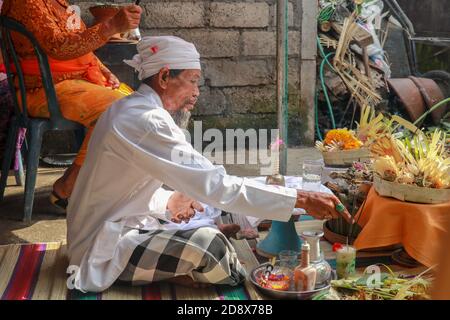 Rückansicht des hinduistischen Priesters, der während einer Hochzeitszeremonie betet. Pedanda sitzt auf dem Boden vor den Opfergaben und führt Hochzeitszeremonien durch Stockfoto
