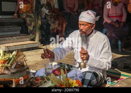 Rückansicht des hinduistischen Priesters, der während einer Hochzeitszeremonie betet. Pedanda sitzt auf dem Boden vor den Opfergaben und führt Hochzeitszeremonien durch Stockfoto