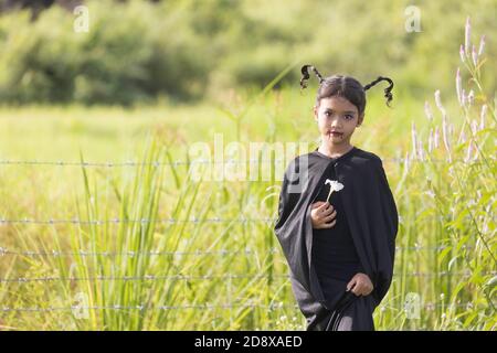 Ein Schulmädchen, ein asiatisches Mädchen gekleidet wie ein Zombie, hält eine weiße Blume in einem Garten. Stockfoto