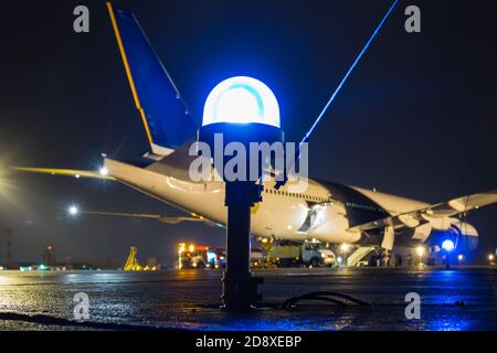 Rollbahn, Seitenreihenbeleuchtung auf dem Hintergrund eines großen Passagierflugzeuges auf dem Vorfeld des Nachtflughafens Stockfoto