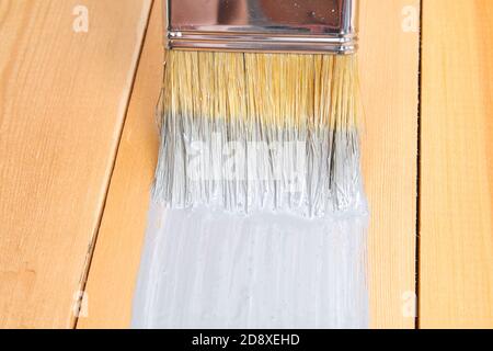 Pinsel mit Dose malen in der Hand. Ein Mann malt Holzbretter mit einem grauen Pinsel. Stockfoto