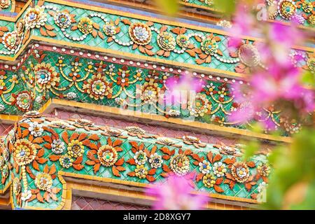 Elegante Blumenmosaikfliesen von Stupa von Wat Pho, Thailand. Rosa Blumen verschwommen im Vordergrund. Stockfoto