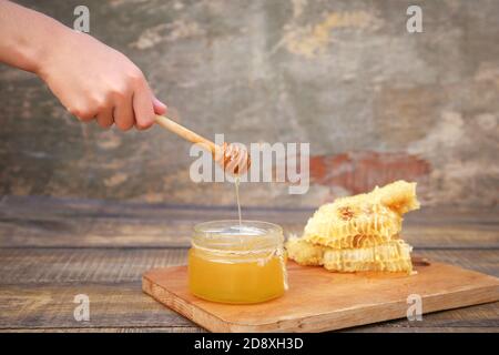 Honig in einem Glas und Wabe auf einem alten hölzernen Hintergrund. Stockfoto