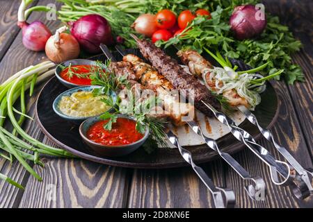 Verschiedene Arten von Hackfleisch/Faschiertem, auf Spießen mit Gemüse auf einem Holztablett. Dieses Gericht heißt lula Kebab. Stockfoto