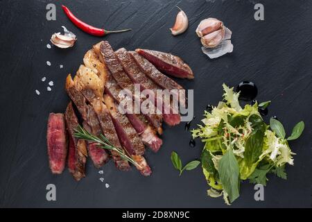 Ein in Scheiben geschnittenes, saftiges Rippenauge auf einem schwarzen Steintisch mit Knoblauch und Chili. Draufsicht Stockfoto