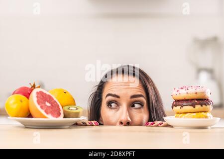 Frisches Obst über ungesunde Donuts Präferenz von einer Frau in der Küche. Stockfoto