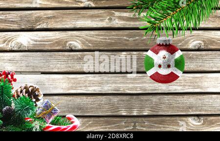 Konzept von Neujahr und Weihnachten, auf einem hölzernen Hintergrund, Christbaumzweige und ein Weihnachtsspielzeug mit der Flagge von Burundi. Stockfoto