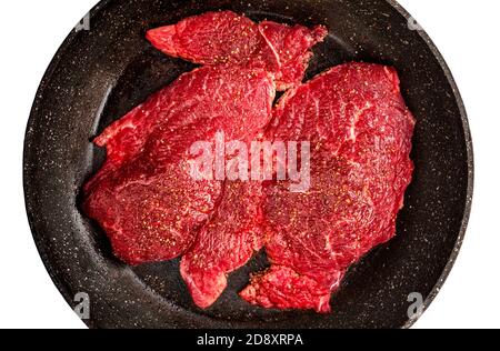 Frisches rohes Rindersteak über schwarzer Bratpfanne isoliert auf weißem Hintergrund, Nahaufnahme. Beste Rindfleisch Fleisch Blick von oben Stockfoto