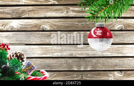 Konzept von Neujahr und Weihnachten, auf einem hölzernen Hintergrund, Weihnachtsbaumzweige und ein Weihnachtsspielzeug mit der Flagge von Singapur. Stockfoto