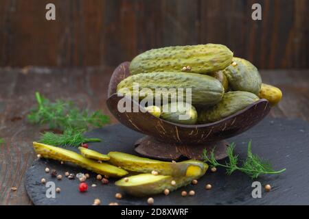 Eingelegte Gurken mit Kräutern und Gewürzen auf Holzgrund. Hausgemachte marinierte Cornichons in einer Schüssel. Stockfoto