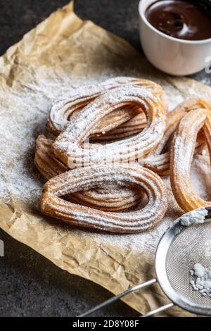 Leckere frittierte Churros mit Zuckerpulver und Schokoladendip auf Geschenkpapier. Stockfoto