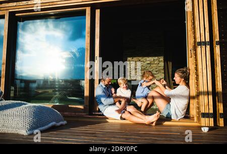 Familie mit kleinen Kindern sitzen auf der Terrasse der Holzhütte, Urlaub in der Natur Konzept. Stockfoto