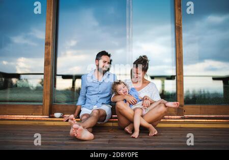 Familie mit kleiner Tochter sitzt auf der Terrasse der Holzhütte, Urlaub in der Natur Konzept. Stockfoto
