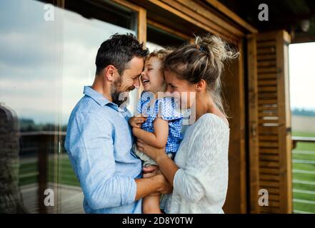 Familie mit kleiner Tochter steht auf Terrasse der Holzhütte, Urlaub in der Natur Konzept. Stockfoto