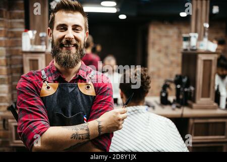 Portrait des fröhlichen jungen barbers mit dem Kunden im Barbershop und lächelnd. Stockfoto