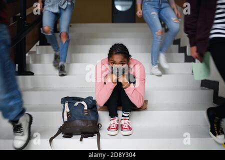 Depressive junge Student mit Gesichtsmaske sitzen auf dem Boden zurück an der Hochschule oder Universität, Coronavirus Konzept. Stockfoto