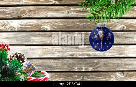 Konzept von Neujahr und Weihnachten, auf einem hölzernen Hintergrund, Weihnachtsbaum Äste und ein Weihnachtsspielzeug mit der Flagge Staat Indiana. Stockfoto