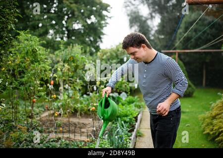 Down-Syndrom Erwachsene Mann Bewässerung Pflanzen im Freien im Gemüsegarten, Gartenkonzept. Stockfoto