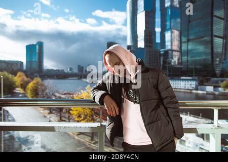 Schöner Casual Mann in schwarzer Jacke und rosa Kapuzenpullover auf einem Wolkenkratzer Blick stehen. Denkkonzept Stockfoto