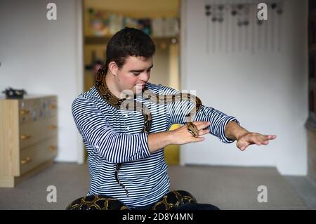 Down-Syndrom erwachsenen Mann sitzt drinnen im Schlafzimmer zu Hause, spielt mit Haustier Schlange. Stockfoto