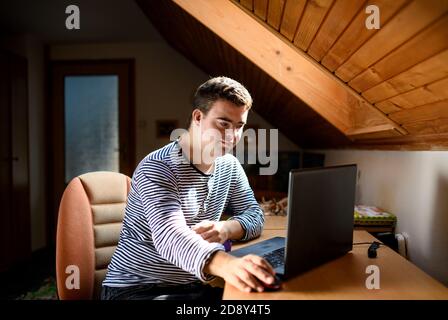 Down-Syndrom erwachsenen Mann sitzt drinnen im Schlafzimmer zu Hause, mit Laptop. Stockfoto