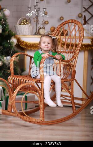 Nettes kleines Mädchen sitzt in Schaukelstuhl in der Nähe weihnachtsbaum Stockfoto