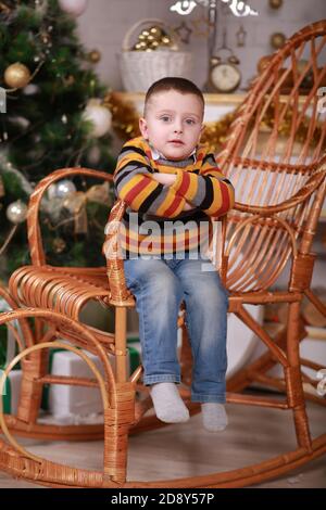 Niedlicher kleiner Junge sitzt in Schaukelstuhl in der Nähe von weihnachtsbaum Stockfoto