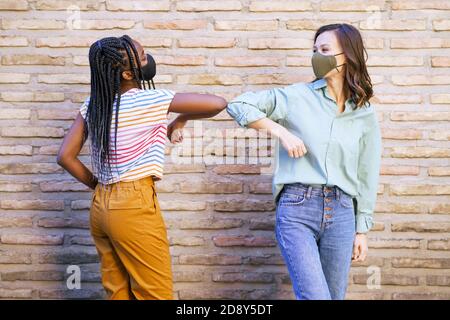 Multiethnische junge Frauen tragen Masken Gruß an einander mit Ihre Ellbogen Stockfoto