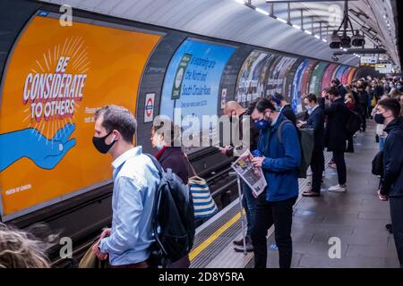 London, Großbritannien. November 2020. Eine Frau hebt ihre Maske, nachdem sie die Kamera gesehen hat - Warnschilder und Ratschläge sind überall - Tragen Sie eine Maske, halten Sie Abstand, seien Sie rücksichtsvoll. Reisende tragen meist Masken, da sie jetzt im öffentlichen Verkehr obligatorisch sind. Die Passagierzahlen sind auf der Tube gestiegen, ebenso wie die Regierung ankündigt, dass am donnerstag eine neue Coronavirus-Sperre (covid 19) beginnt. Kredit: Guy Bell/Alamy Live Nachrichten Stockfoto