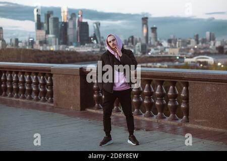 Schöner Casual Mann in schwarzer Jacke und rosa Kapuzenpullover auf einem Wolkenkratzer Blick stehen. Dämmerung. Stockfoto