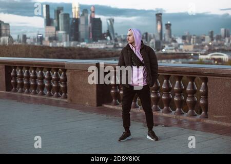 Schöner Casual Mann in schwarzer Jacke und rosa Kapuzenpullover auf einem Wolkenkratzer Blick stehen. Dämmerung. Stockfoto