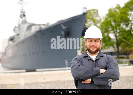 Porträt des Kapitäns der Marine, der in der Nähe eines großen Schiffes im Hintergrund steht. Stockfoto