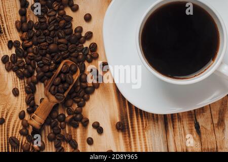 Leckere Tasse Kaffee. Frisch geröstete Kaffeebohnen in Holzlöffel und Tasse Kaffee auf Holzhintergrund. Rustikaler Stil. Stockfoto