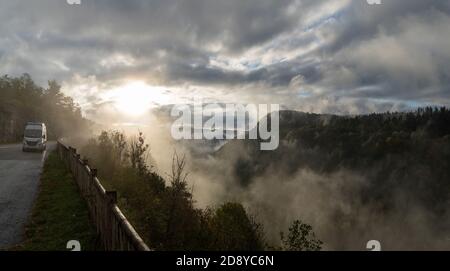 Ein geparkter Wohnmobil mit wunderschönen Herbstfarben Wald und Berglandschaft im Nebel und Nebel bei Sonnenaufgang Stockfoto