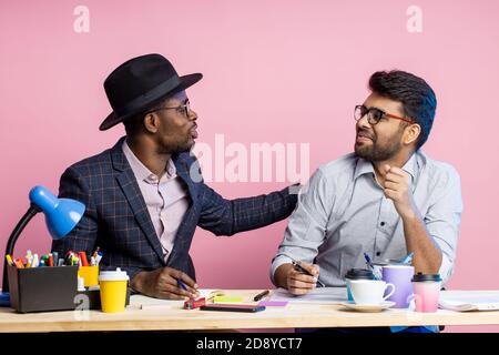 Zwei Kollegen arbeiten zusammen, diskutieren über neues Projekt, erstellen Finanzbericht, halten Stifte, sitzen am Büroschreibtisch, tragen formelle Kleidung, Brille, Stockfoto