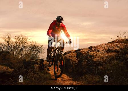 Radler in Red Riding Bike auf dem Herbst Rocky Trail bei Sonnenuntergang. Extreme Sport und Enduro Biking Konzept. Stockfoto