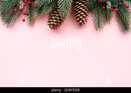 Grüner Schaum Weihnachtsbaum Ast Grenze mit Zapfen und rot Beeren auf dem rosa Hintergrund Stockfoto