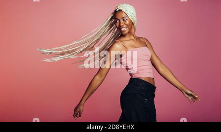 afroamerikanische Frau mit langen geflochtenen Haaren Blick über ihre Schulter. Lächelnde Frau, die ihre Haare auf rosa Hintergrund herumfliegt. Stockfoto