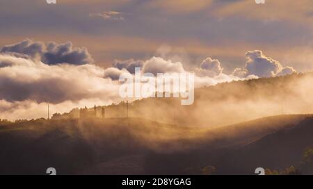 Sonnenaufgangslicht bedeckt die lockigen Wolken, die über Wiesen und Felder laufen und ein magisches Licht-Schatten spielen. Schöne Hügel der Toskana neblig Morgen la Stockfoto