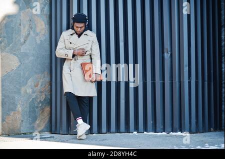 Afroamerikanischer Mann mit Kopfhörern, tragen Hut und Mantel hören Musik auf Stahl Hintergrund. Stockfoto