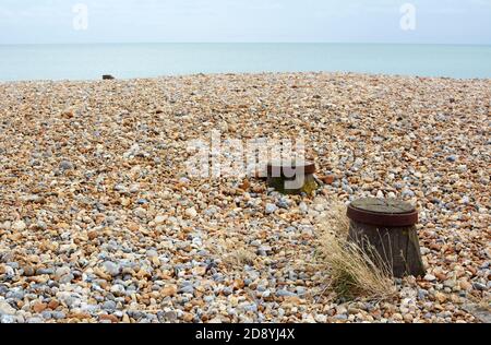 Kiesstrand an der englischen Küste mit hölzernen Groyne-Gipfeln Aus den grauen und braunen Steinen hervorgegangen Stockfoto