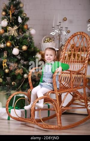 Nettes kleines Mädchen sitzt in Schaukelstuhl in der Nähe weihnachtsbaum Stockfoto