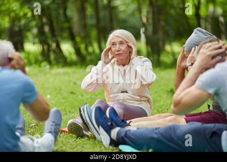 Eine Gruppe moderner Senioren hat sich im Park versammelt Auf Matten auf Gras tun Hals Stretching entspannende Übung Stockfoto