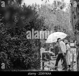 Straßburg, Frankreich - 1. Nov 2020: Seniorenpaar mit Regenschirm betritt den Friedhof in Frankreich am Allerheiligen während der zweiten Welle des Coronavirus - monochromes Bild Stockfoto