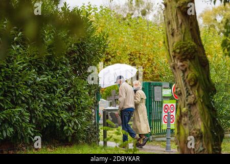 Straßburg, Frankreich - 1. Nov 2020: Seniorenpaar mit Regenschirm, das während der zweiten Welle des Coronavirus in Frankreich am Allerheiligen-Tag auf den Friedhof kommt Stockfoto