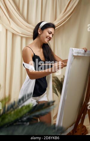 Junge lächelnde Künstlerin vor Staffelei. Frau Malerei im Kunststudio Stockfoto