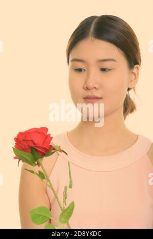 Nahaufnahme der jungen schönen asiatischen Frau halten und Blick auf rote Rose Stockfoto